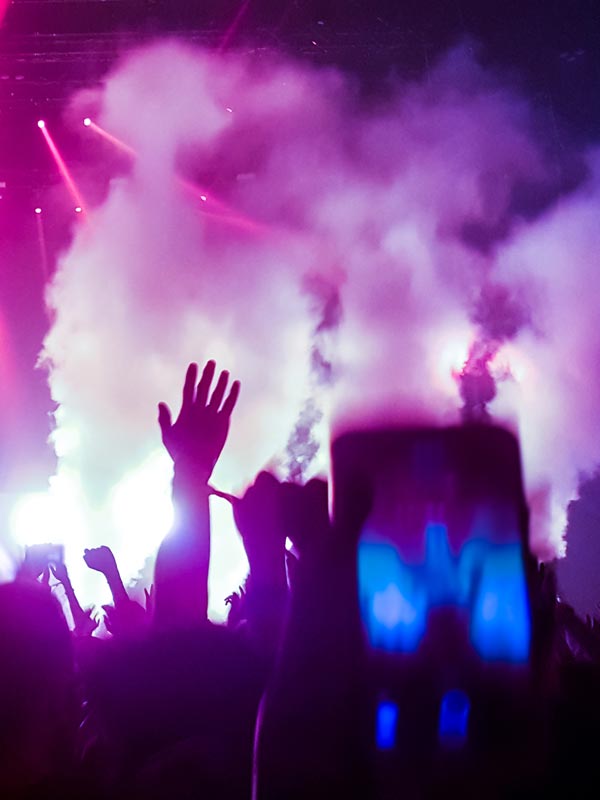 A crowd of people at a music event using smoke machines and stage lighting.