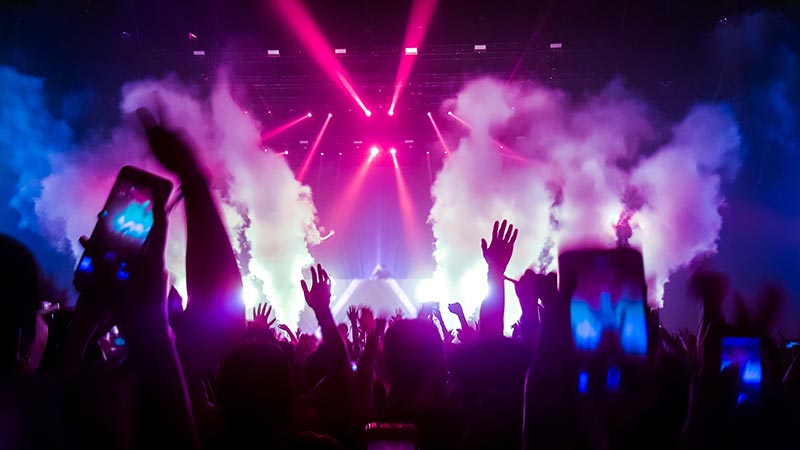 A crowd of people at a music event using smoke machines and stage lighting.